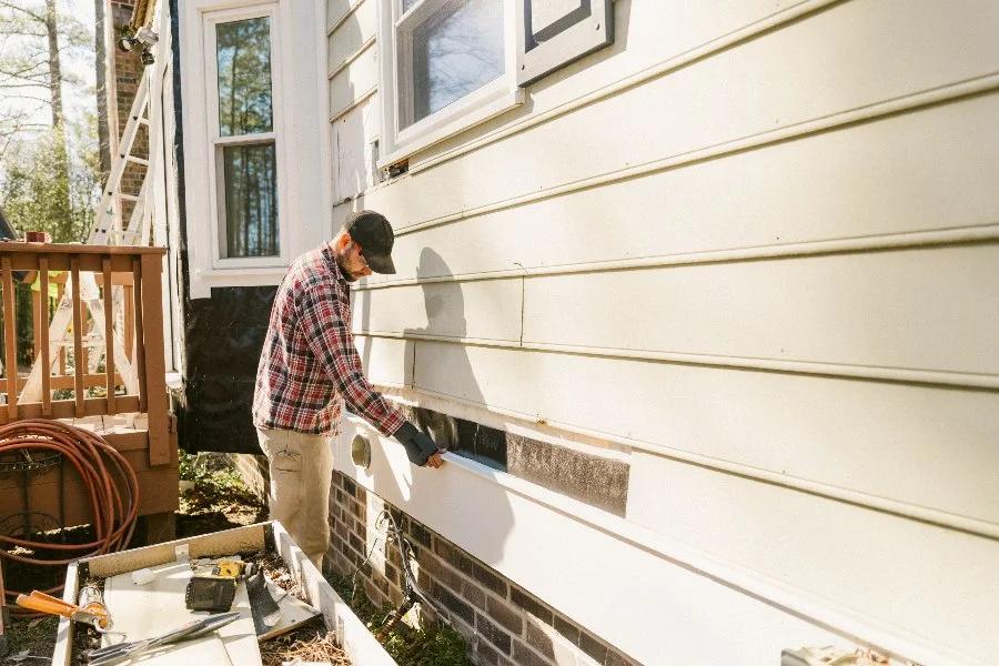 A man refacing the exterior of a house by Modular Home Additions.