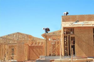 Construction workers installing roofing materials on a house under a clear blue sky.