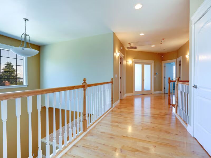 A hallway featuring hardwood floors and white railings, creating a bright and inviting atmosphere.